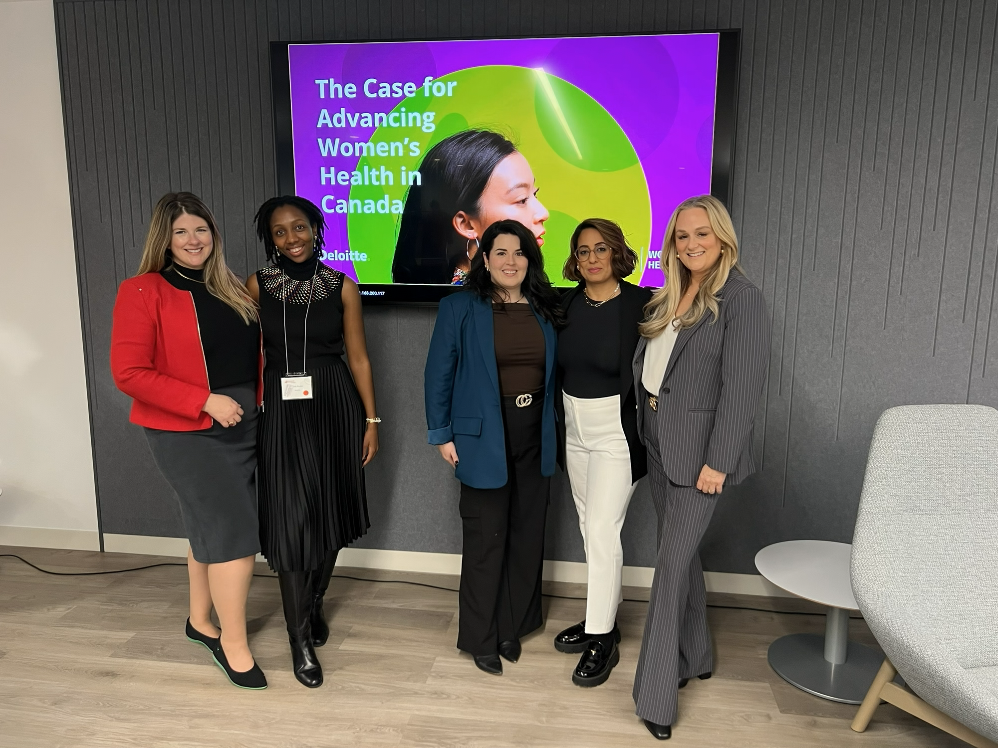 Five women standing together in front of a presentation screen titled “The Case for Advancing Women’s Health in Canada,” posing in professional attire in a modern conference room.