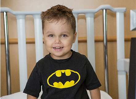 Zaccari laying in a hospital bed with a batman t-shirt on and a smile on his face