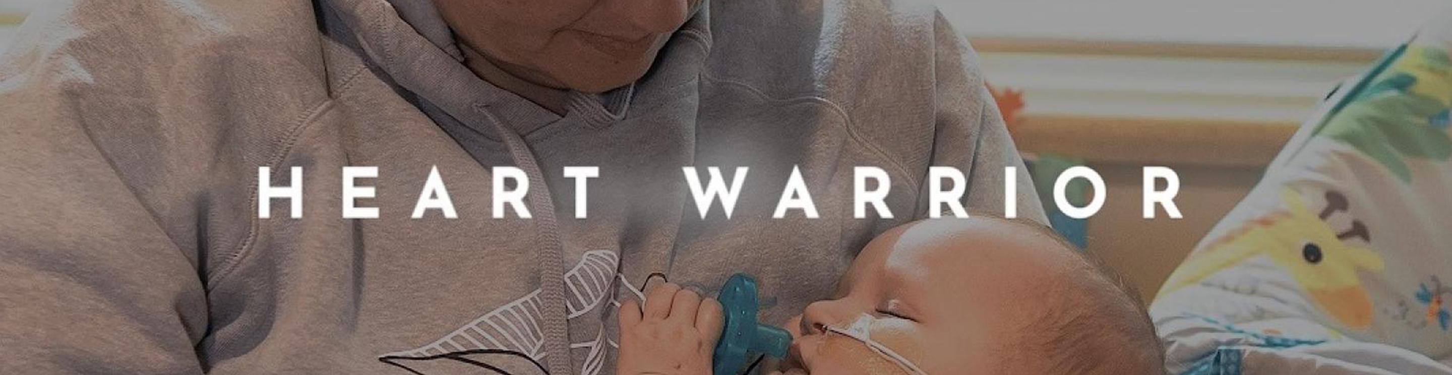 A mother holding a baby boy with a soother in his mouth. The words Heart Warrior overlay the image.