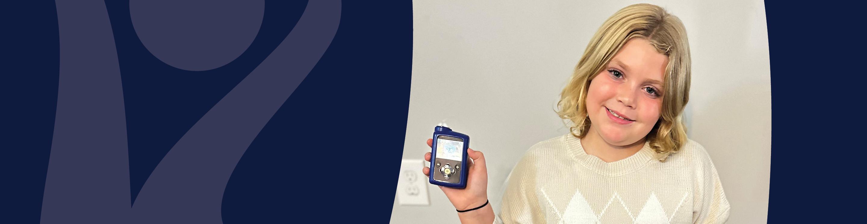 Charlie wearing a cream sweater holds a small blue handheld medical device while standing against a light-colored wall. A dark blue graphic design fills the left side of the image.