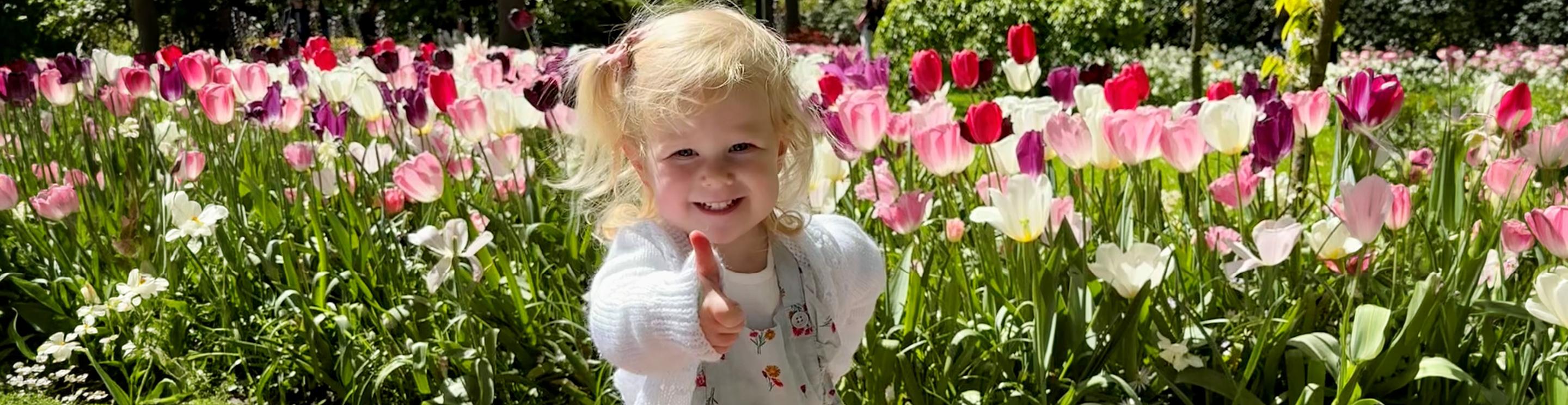 Marigold giving a thumbs-up while standing among colorful pink, white, and purple tulips in a sunny garden.