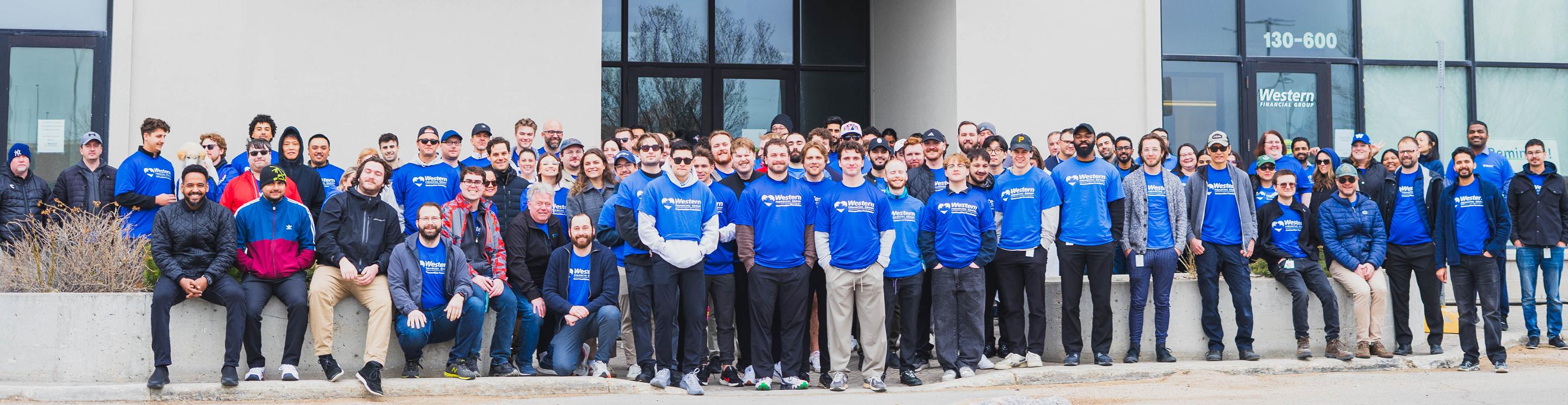 A large group of employees wearing matching blue shirts pose outside Western Financial Group's office building.