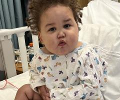 William, IWK patient, sitting on a bed eating breakfast.