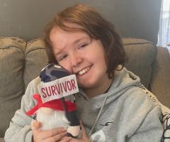 IWK patient, Jeric, holding a stuffed toy with a "survivor" banner.