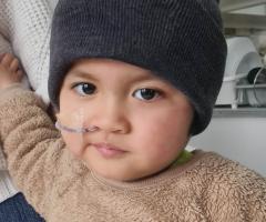 Johnny receiving hospital care, alongside a close-up with a nasal tube holding an adult’s hand.