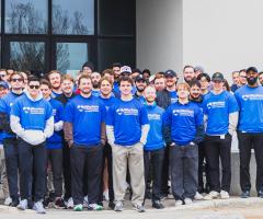 A large group of employees wearing matching blue shirts pose outside Western Financial Group's office building.