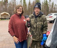 Community fishing derby participants gather outdoors, pose with trophies, and display a prize-winning fish.