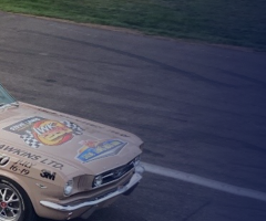 Vintage Mustang pace car carrying passengers waving a Canadian flag beside the IWK 250 event logo.