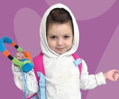Kenza in a white hoodie holding colorful headphones, standing against a purple background.